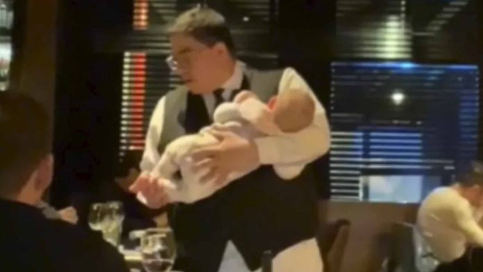 Mesero se viraliza por cargar a un bebé mientras atiende a los comensales